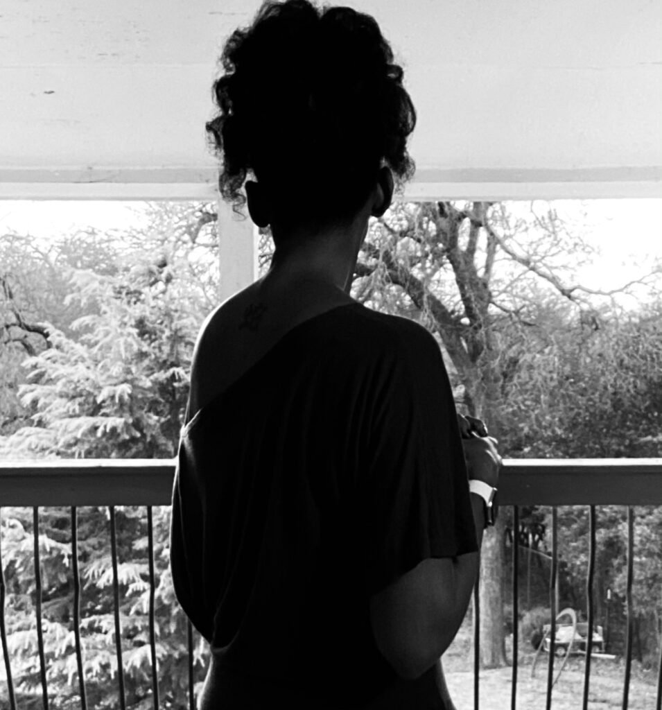 Woman facing away from the camera standing on a balcony overlooking trees