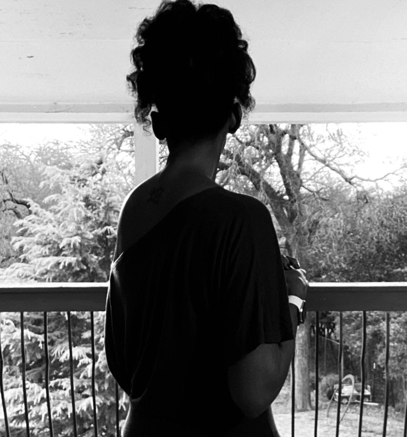 Woman facing away from the camera standing on a balcony overlooking trees