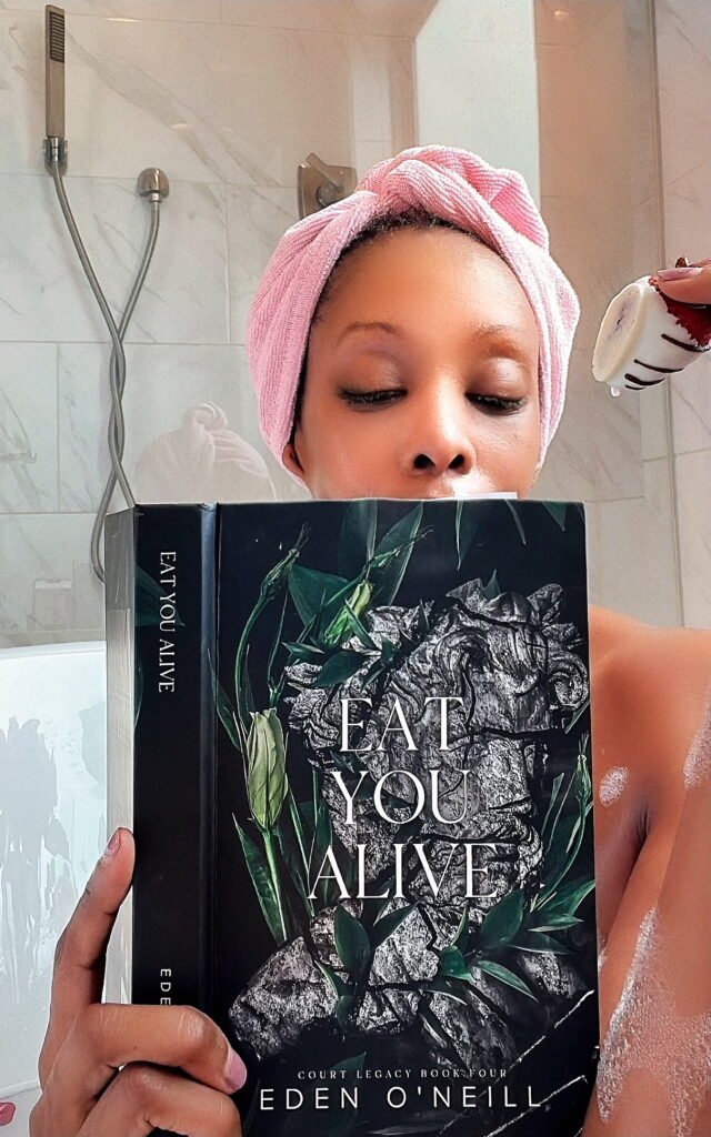 woman in a bathtub reading a book and eating a chocolate covered strawberry
