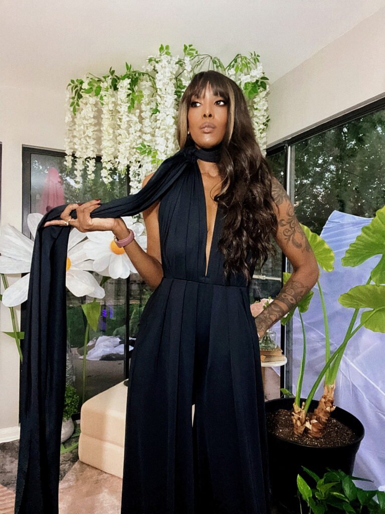 Woman in a black jumpsuit surrounded by green plants