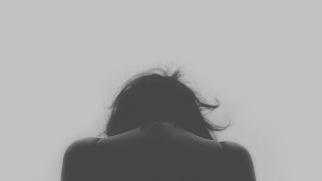greyscale photo of woman's back as she hangs her head to pause