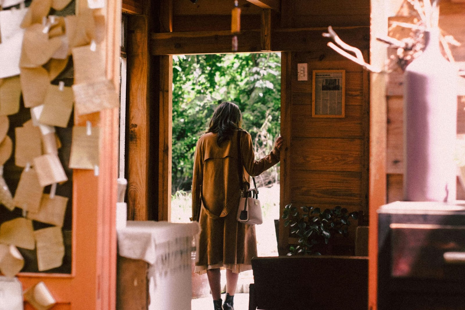 A woman in a warm coat steps out of a cozy cabin into the sunlight.