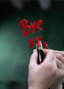 Handwriting 'bye' on a mirror with red lipstick, evoking themes of farewell and emotion.