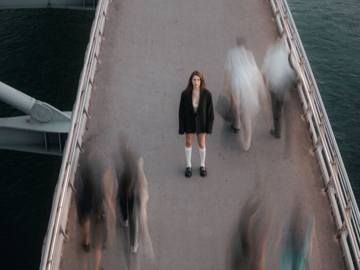 A woman stands still among moving crowds on a city bridge, creating a striking contrast.
